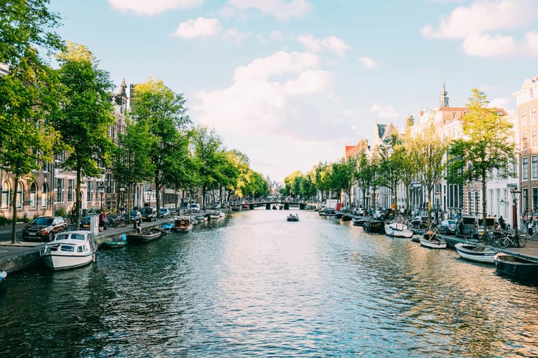 Boats moored along a tree-lined canal with historic canal houses in Amsterdam