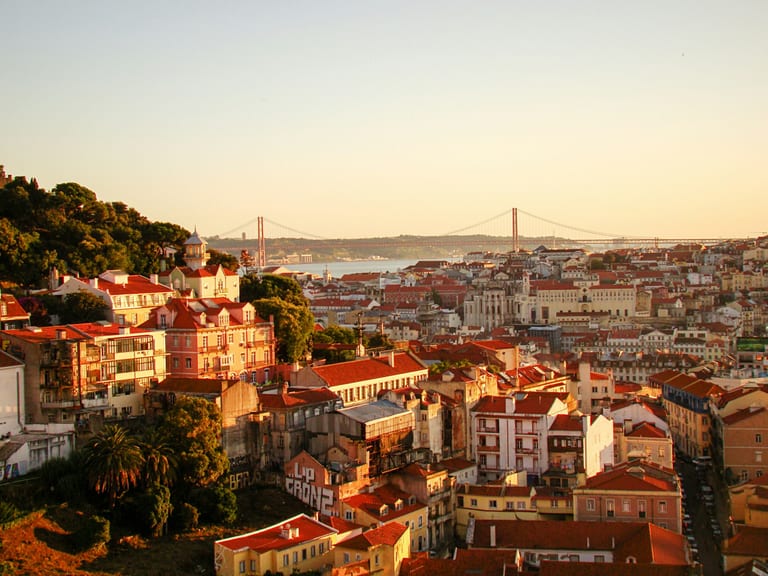 Lisbon rooftops at golden hour with the 25 de Abril bridge over the Tagus in the background